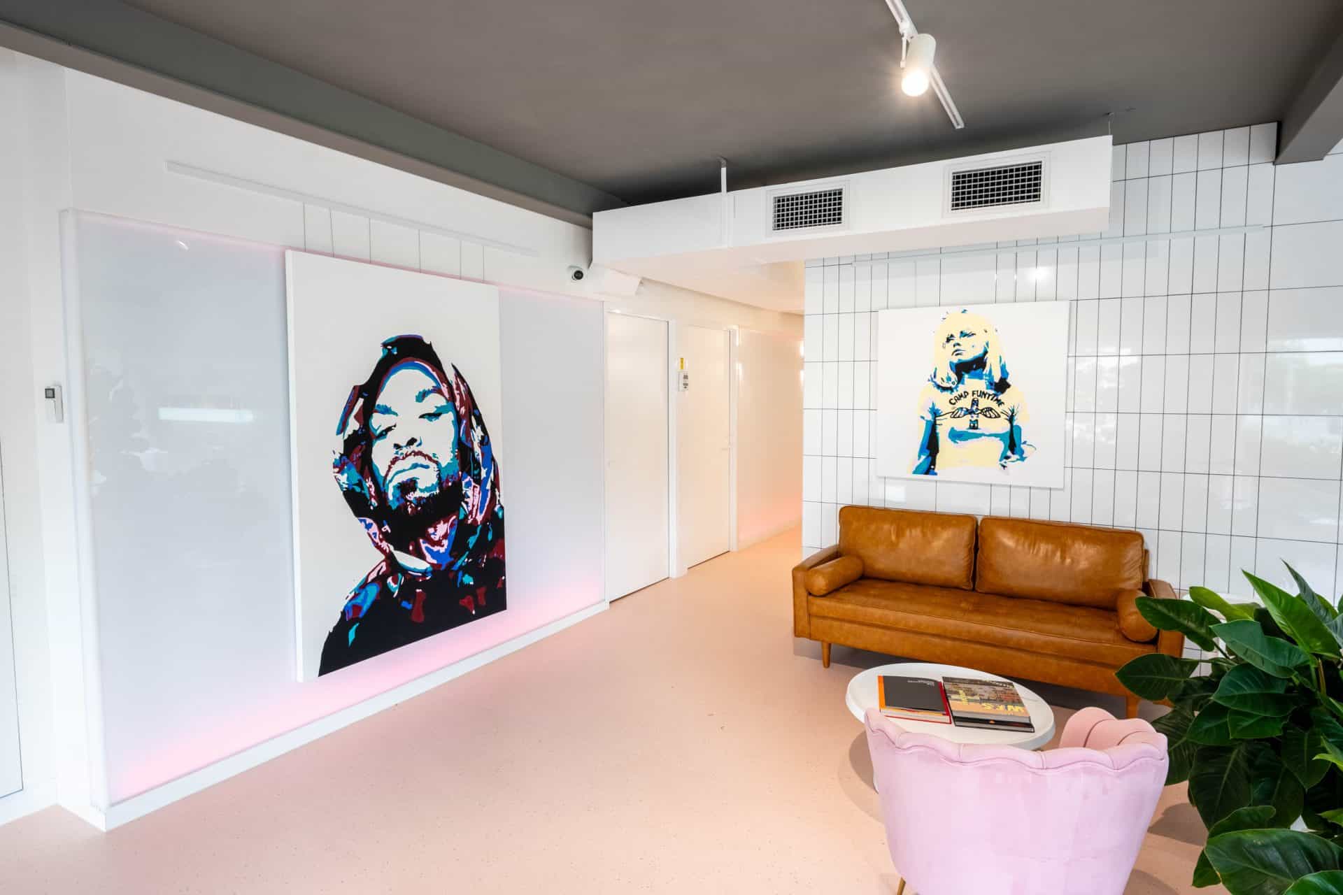 The waiting lounge: a tan leather sofa and pink velvet chair against a white tiled wall hung with pop-art portraits