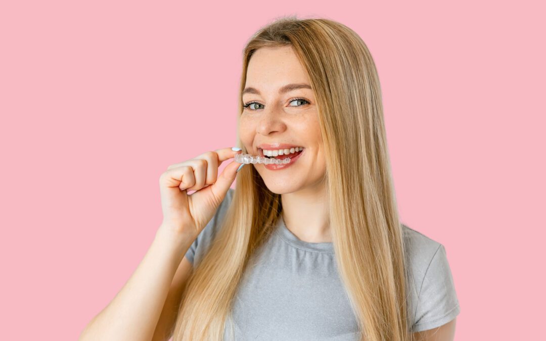 Blonde woman with long hair holding an invisible braces tray in her hand near her mouth.