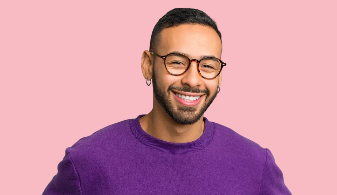 Man with short cropped hair wearing glasses and a bright purple jumper. He has an earring in his ear.