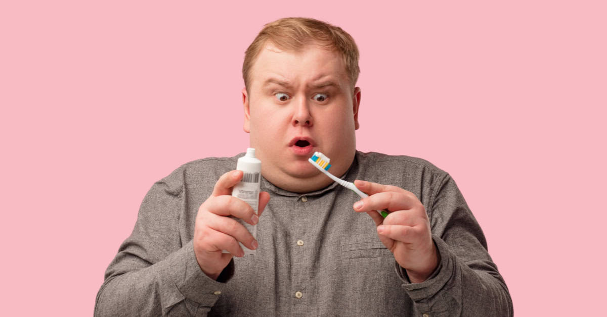 A man holding a toothbrush and a tube of toothpaste.